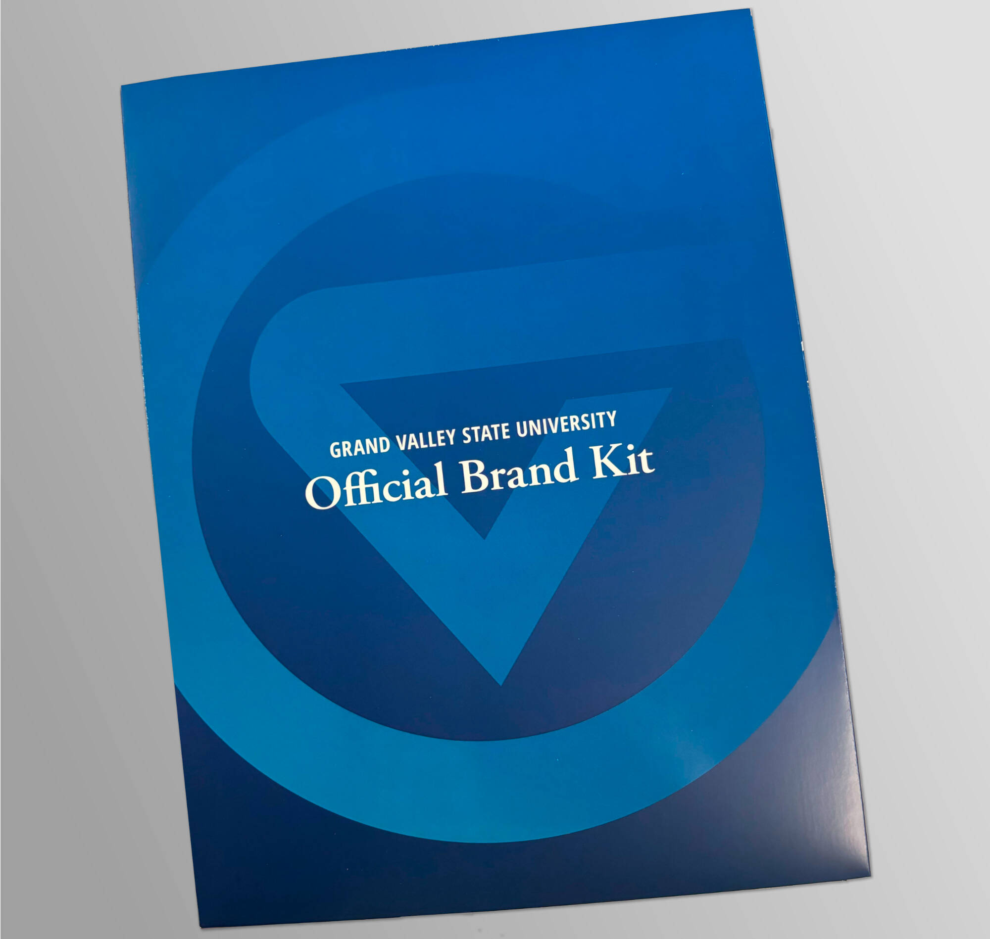 A blue folder with the university's logo mark and the words Official Brand Kit on it.